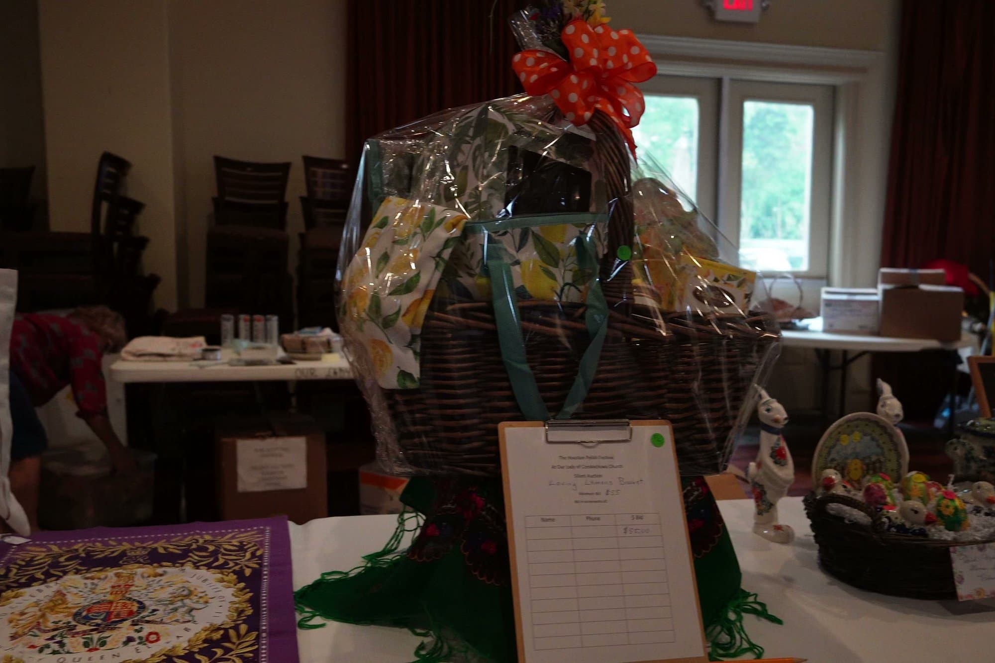 A large wicker hamper wrapped in cellophane with a red bow, its bid sheet propped on a clipboard in front of it.