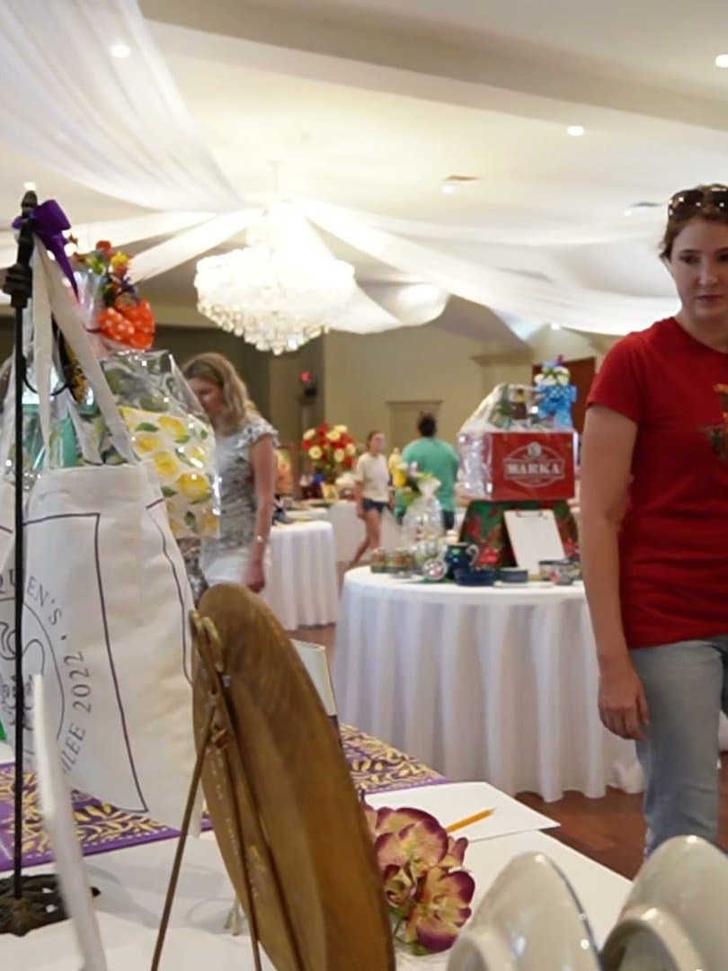 A display stand of donated jewellery and ornaments beside the auction tables, with visitors browsing behind.