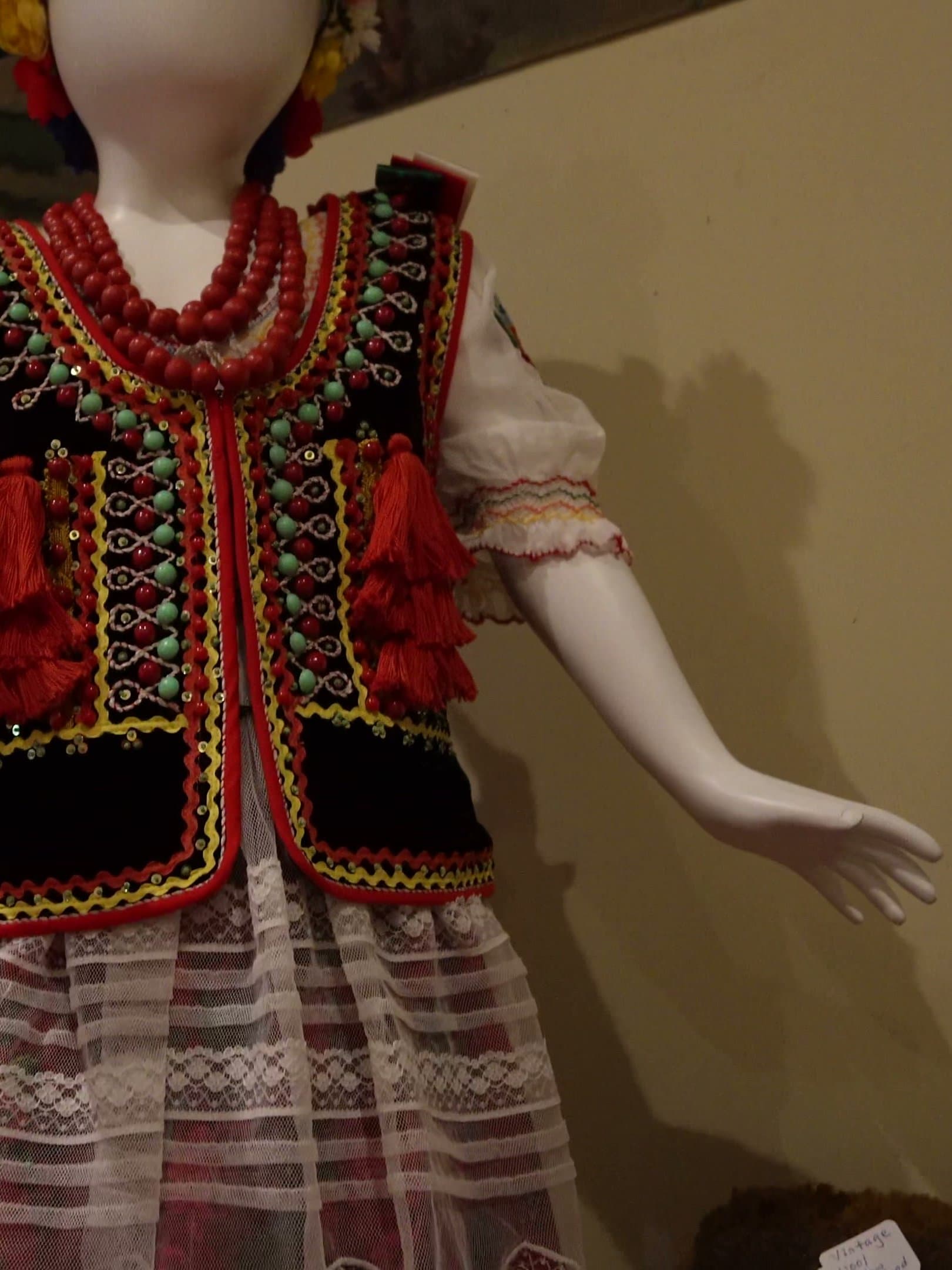 A mannequin dressed in Kraków folk costume: a black velvet bodice edged in gold braid and coloured tassels, layers of red coral beads, and an embroidered white blouse.